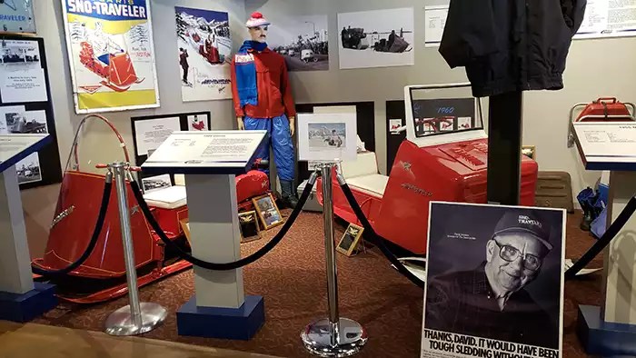 Foreground hs a picture of Dvid Hetteen, with two vintage red Polaris Sno-Travelers in the background. 