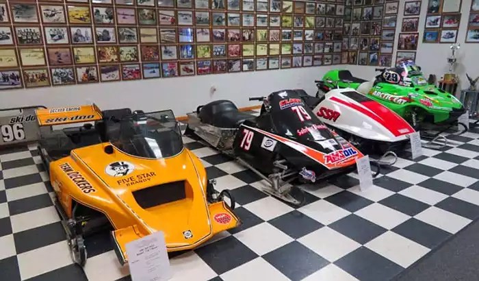 4 Race sleds under a wall of framed photos. 