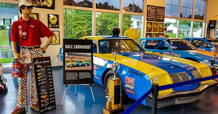 A mannequin stands next to the #2 blue and yellow car driven by Dale Earnhardt. 