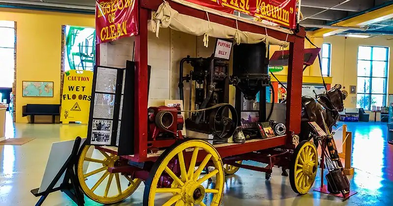 Tall red horse-pulled wagon containing "Puffing Billy" the world's first vacuum. 