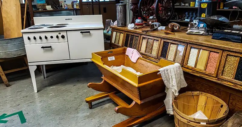 Variety of artifacts including large tin washtub, old electric stove, baby cradle, and more. 