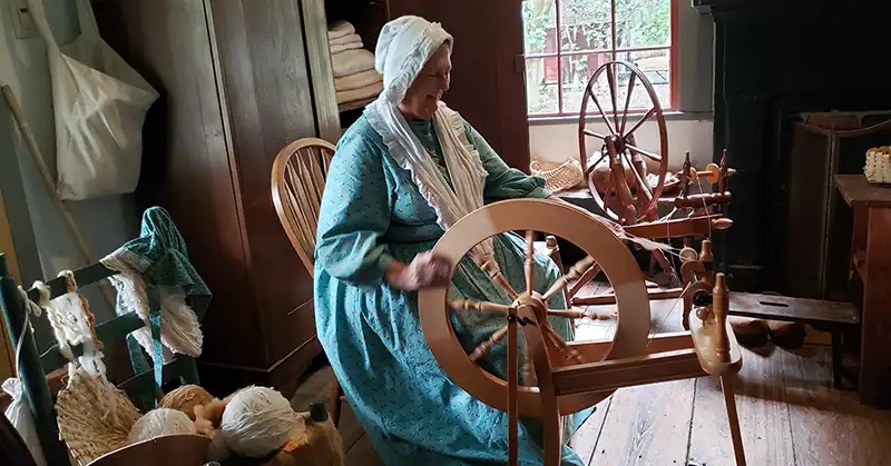 Woman in pioneer-era clothing operating a spinning wheel. 