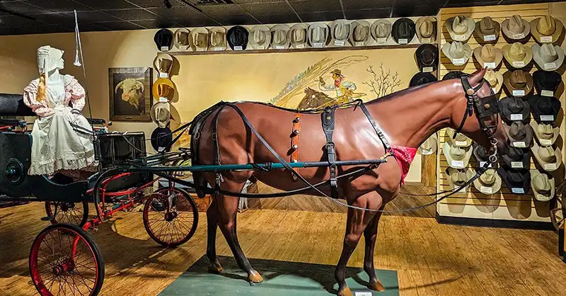 Horse and buggy with a display of cowboy hats and a western mural of a cattle drive. 