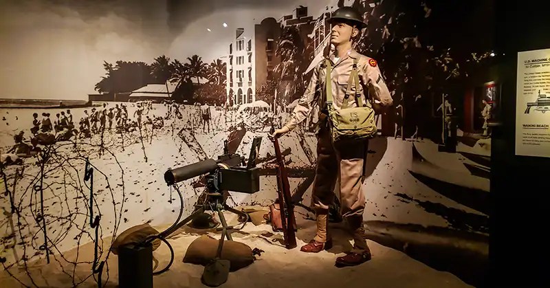 Soldier with a photo backdrop of barbed wire strung around Waikiki beach. 