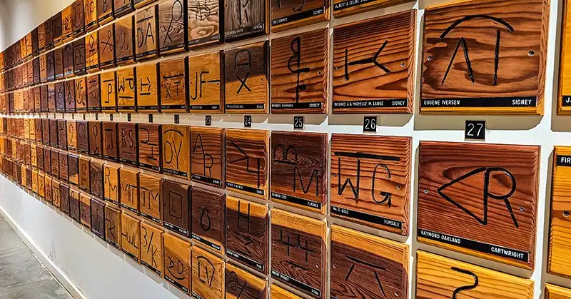 Wall covered with wooden placards providing area brands along with the name and location of the brand owner.