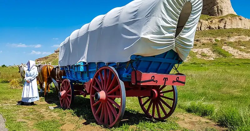 Costumed interpreter with a covered wagon at a living history program.