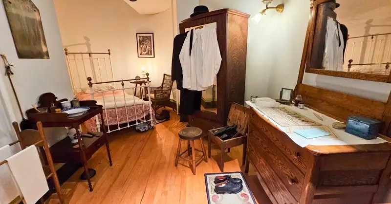 Butler's room in the Maymont Mansion with the cast iron bed, simple furnishings and black work suit. 